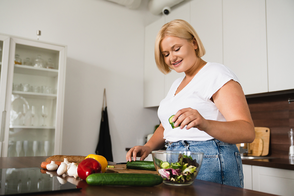 Eine junge Frau bereitet sich in de Küche einen Salat zu.