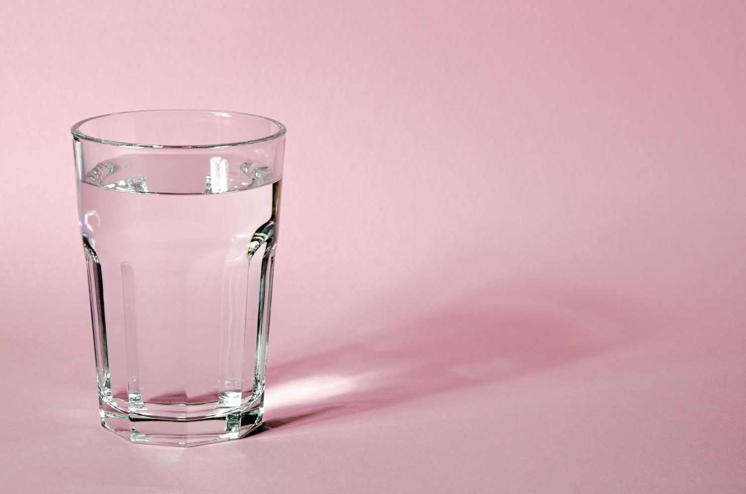 Ein Wasserglas vor rosa Hintergrund